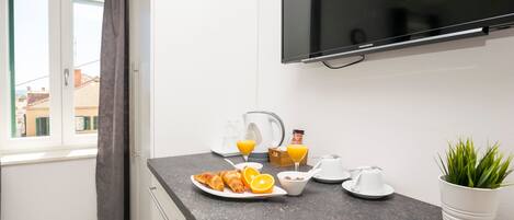 A modern kitchen with a flat-screen TV, breakfast items, and a potted plant.