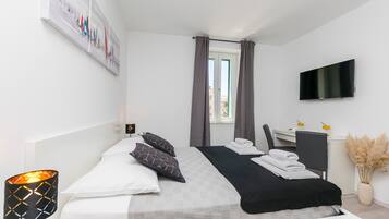 Une chambre d’hôtel moderne équipée d’un lit, d’un bureau, d’une télévision et d’une fenêtre avec des rideaux.