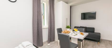 Una habitación moderna y luminosa con una mesa de comedor, sillas, un sofá, un televisor de pantalla plana y una ventana con cortinas.