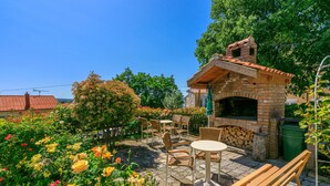 Een terras buiten met een bakoven, zitplaatsen en een tuin met verschillende bloemen.