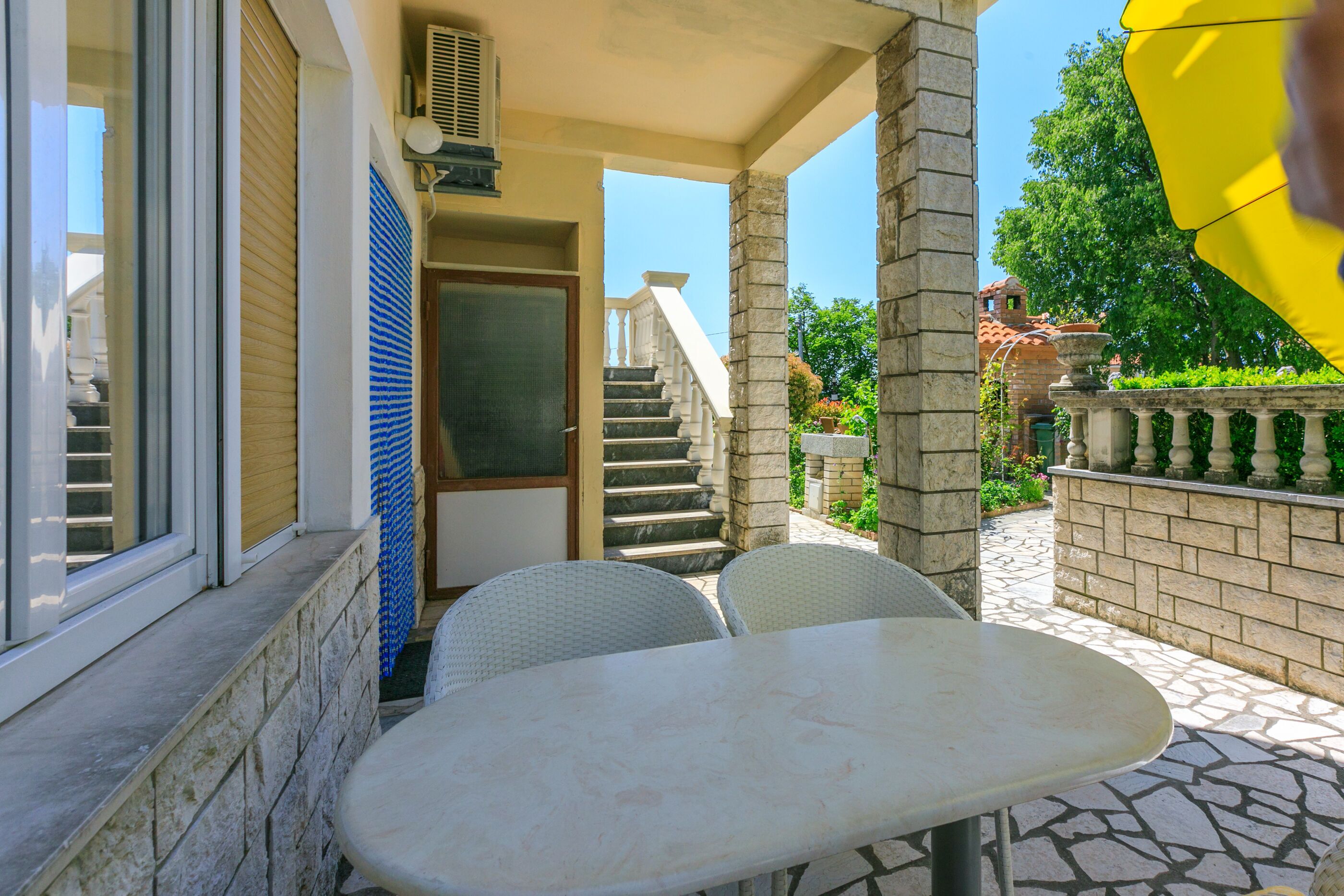 Un'area patio con tavolo e sedie, una porta e una scala che conduce a un livello superiore.
