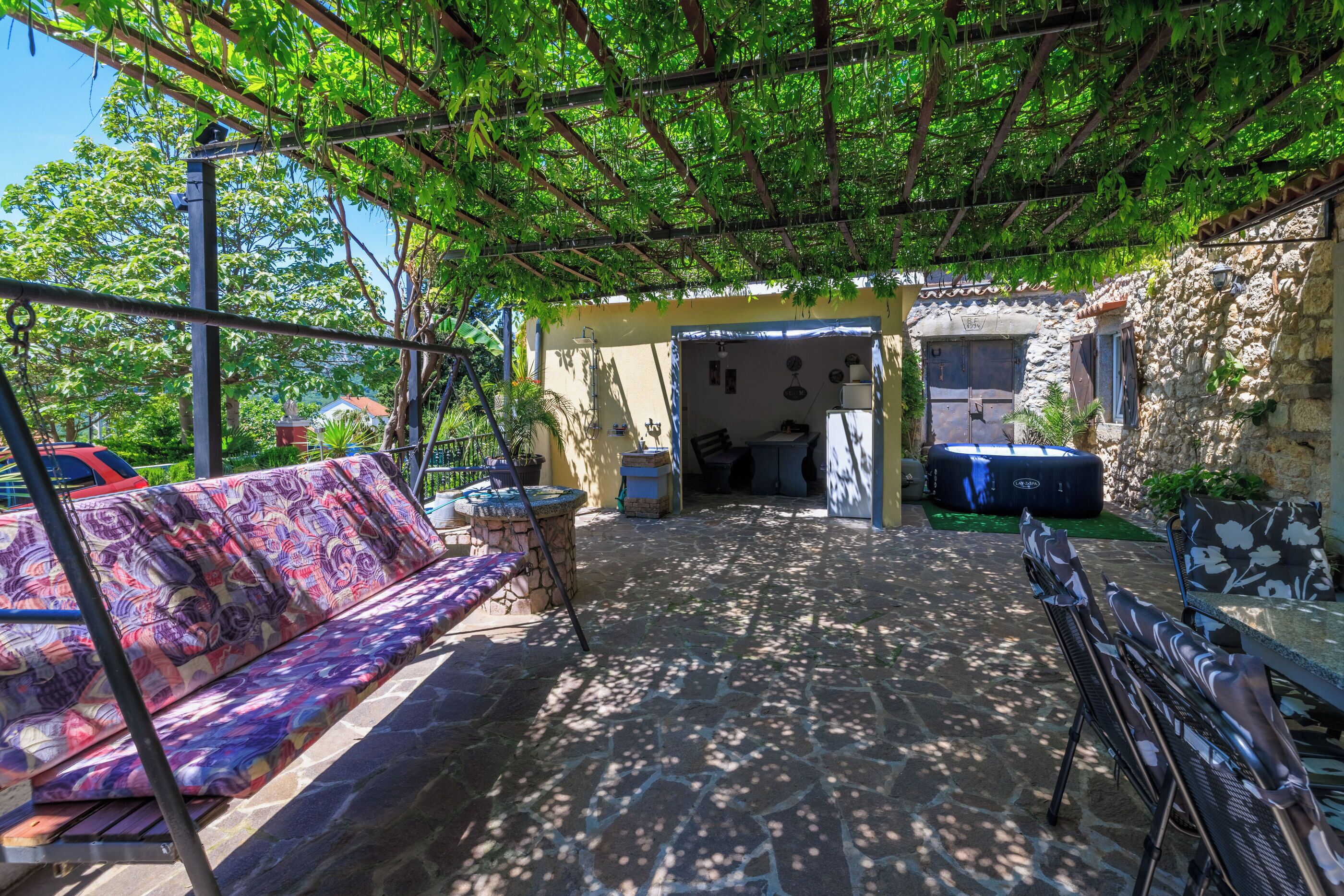 Eine Außenpatio mit Steinboden, einem überdachten Sitzbereich mit gemusterten Kissen und einer Steinwand.