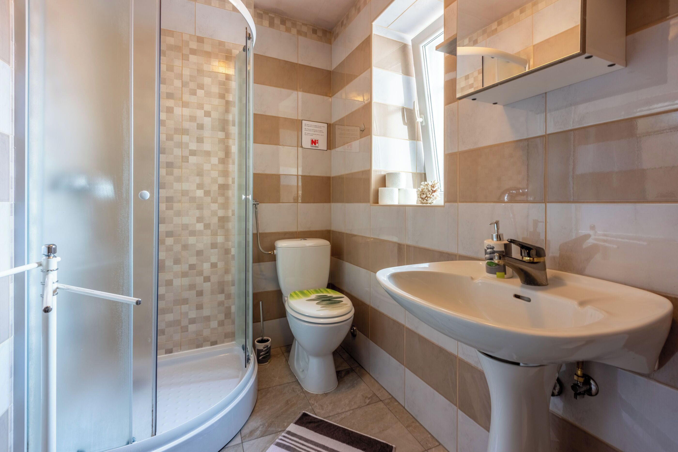 Ein Badezimmer mit einer gläsernen Duschkabine, einer Toilette mit grünem Deckel und einem weißen Waschbecken.
