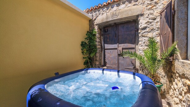 An outdoor hot tub with a stone wall and a wooden door in the background. - House Sevgi (Bribir)