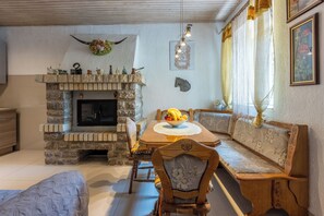 A cozy living room with a stone fireplace, wooden furniture, and a dining table set with fruit. - House Sevgi (Vinodol)