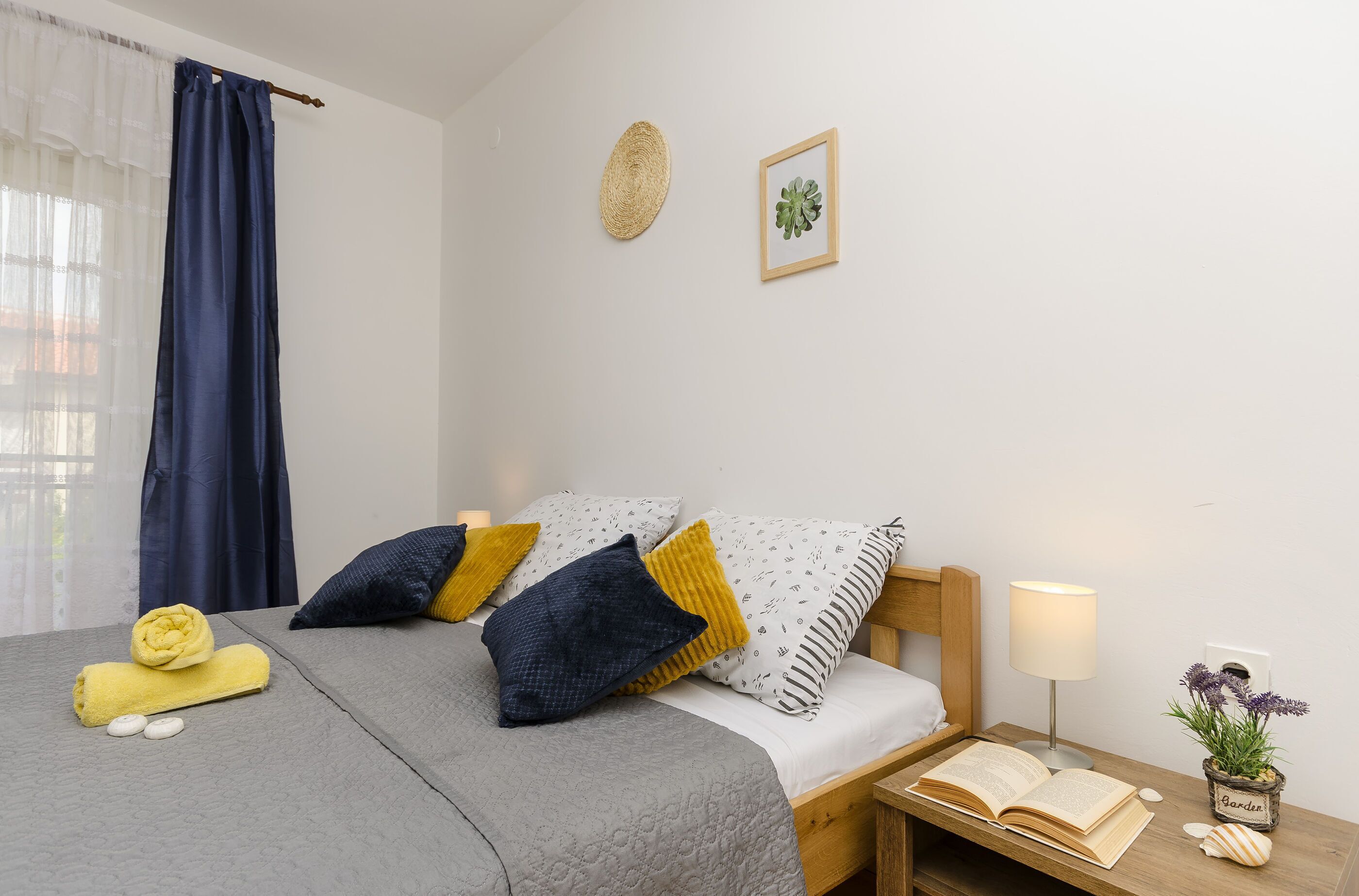 A neatly arranged bedroom with a bed, pillows, a bedside table with a lamp, and a small potted plant.