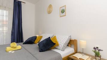 A neatly arranged bedroom with a bed, pillows, a bedside table with a lamp, and a small potted plant.