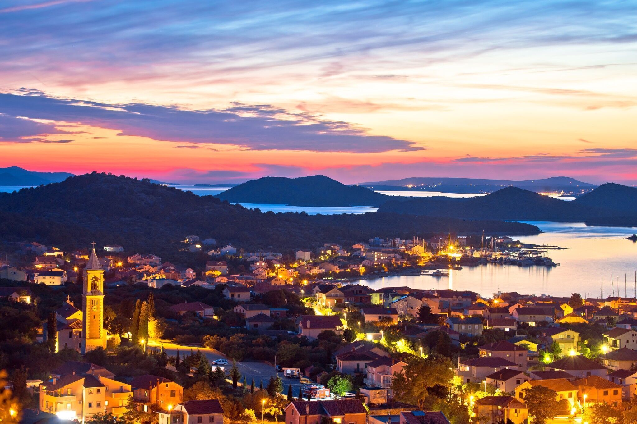 A coastal town at dusk with a prominent church tower, waterfront, and residential buildings.