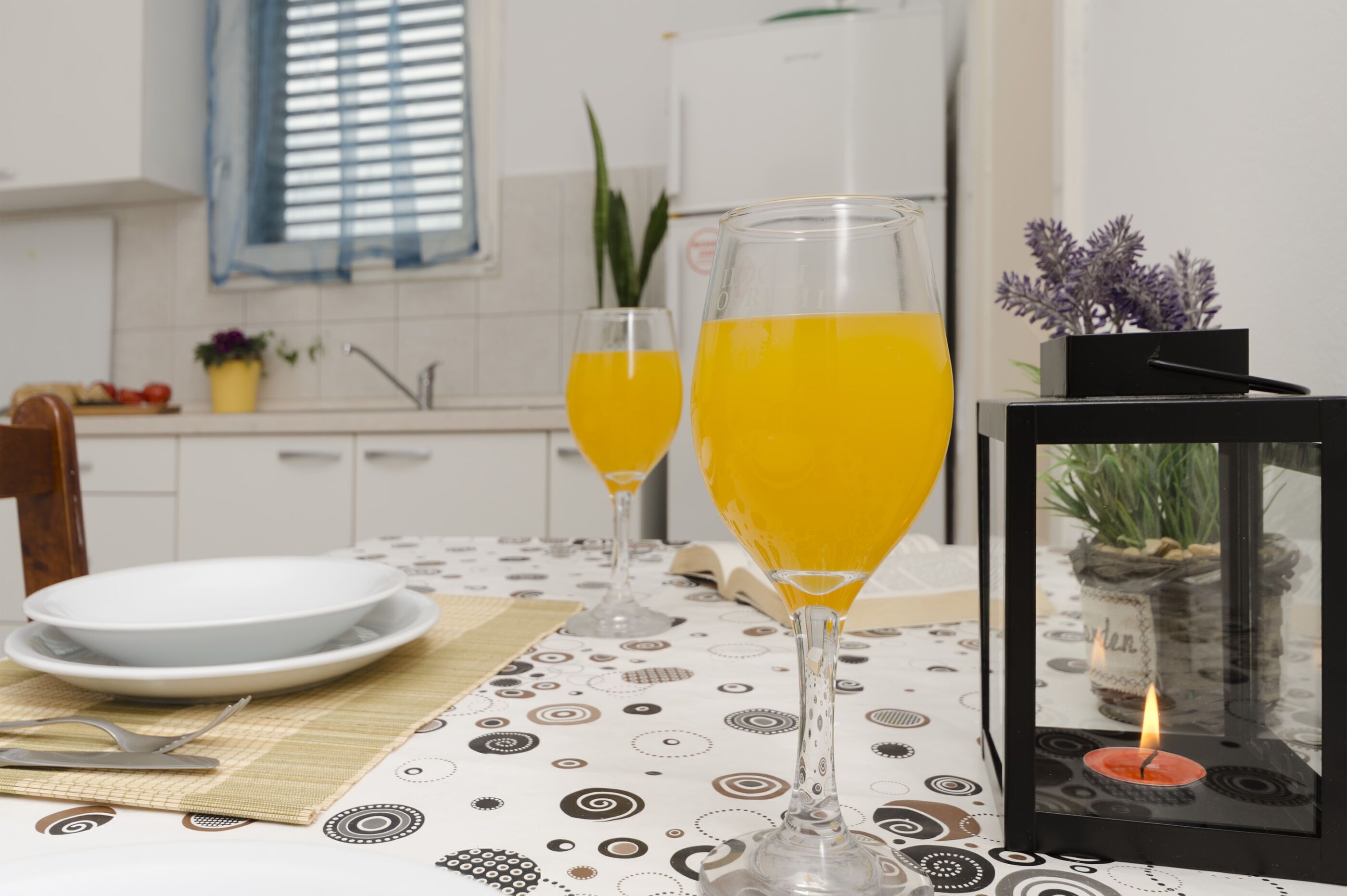 A dining table with two glasses of orange juice, a candle, and a framed plant.