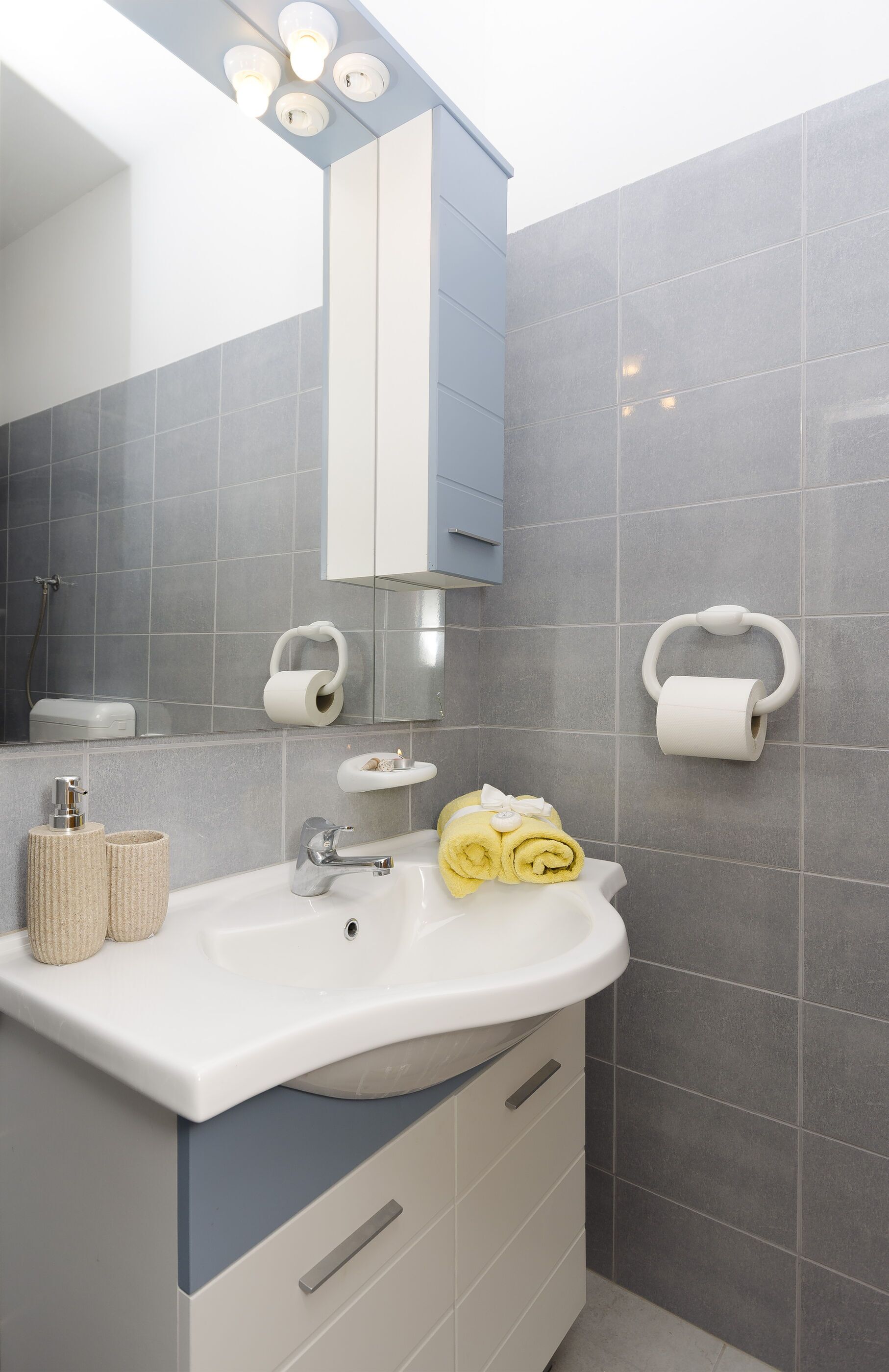 Casa de banho com lavatório branco, espelho e porta-toalhas.
