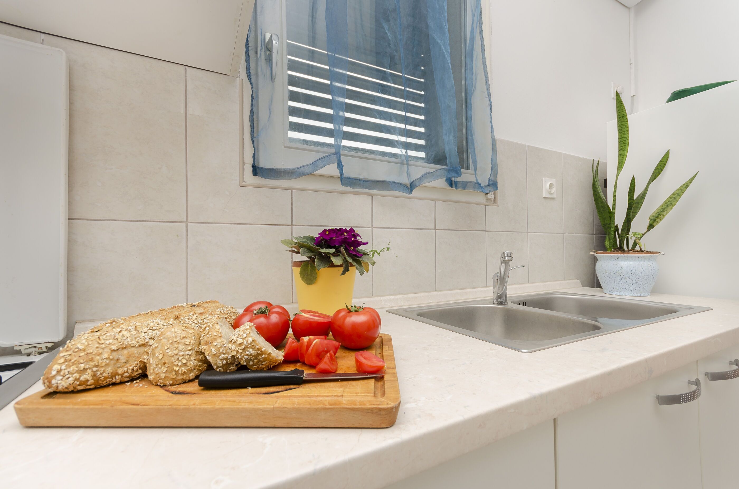 Una cocina con tabla de cortar, tomates, pan y un lavabo.