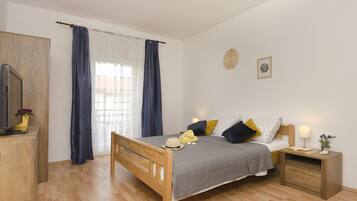 A bedroom with a wooden bed, a bedside table with a lamp, a small wooden dresser, and a window with curtains.