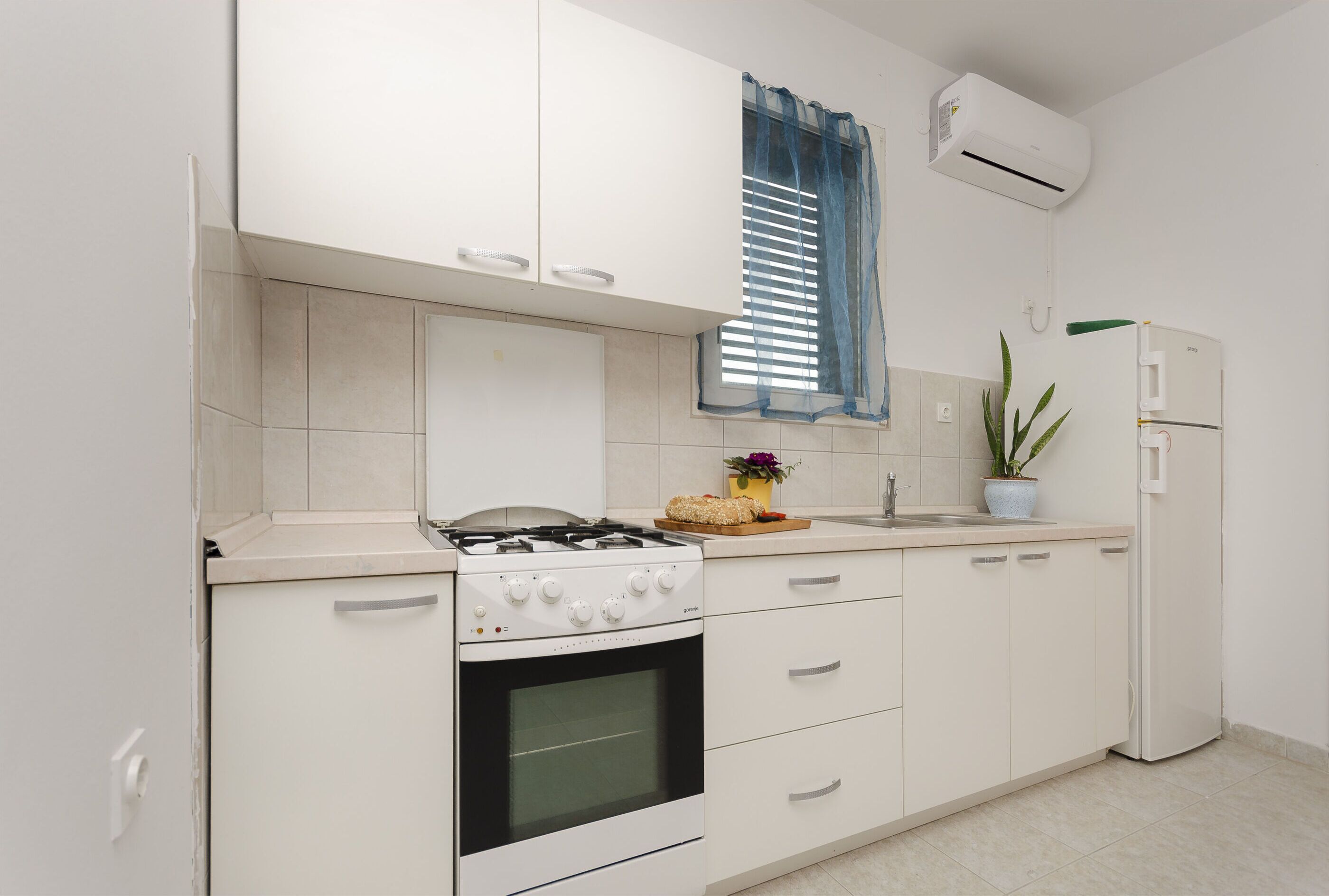 Une cuisine avec des meubles blancs, une cuisinière à gaz, un four, un évier et un réfrigérateur.