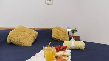 Una cama bien hecha con almohadas mullidas, una mesita de noche con una lámpara, un cuadro enmarcado en la pared y una bandeja con zumo de naranja, fresas y bollería.