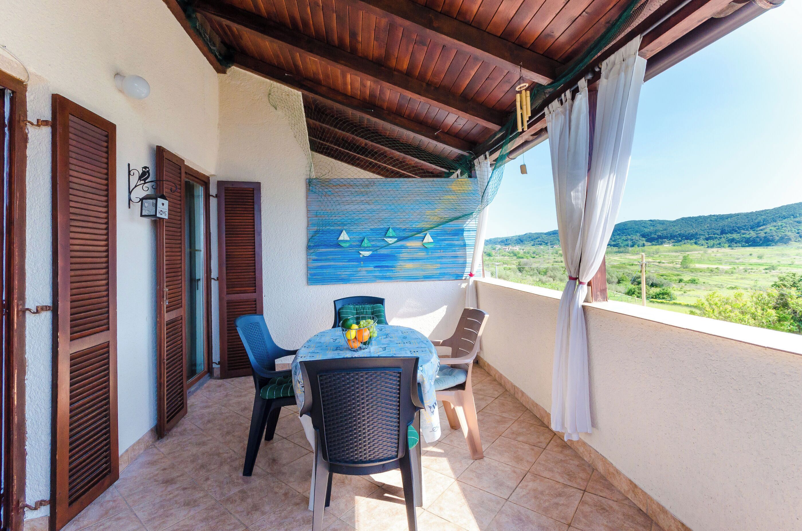 A balcony with a table and chairs, a view of the countryside, and wooden shutters.