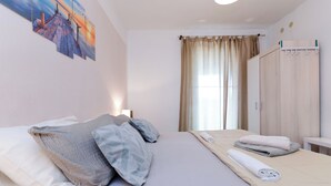 Un lit bien fait, avec des oreillers, une table de chevet sur laquelle est posée une serviette enroulée, une armoire et un tableau accroché au mur.