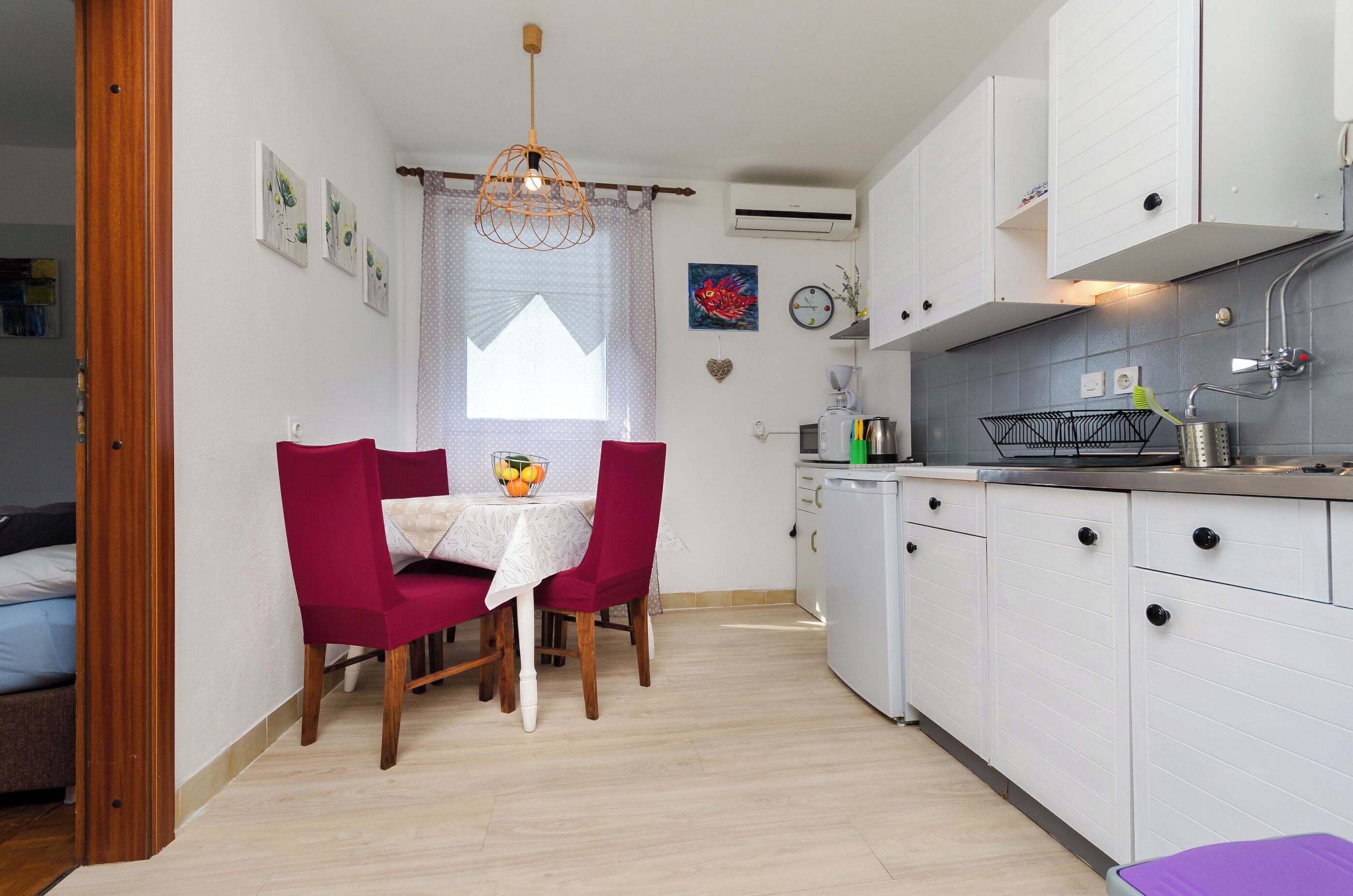 Une cuisine de taille réduite avec des meubles blancs, une table à manger et deux chaises, ainsi qu’un luminaire suspendu.