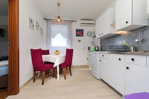 Une cuisine compacte avec des meubles blancs, une table à manger avec des chaises rouges et un petit réfrigérateur.
