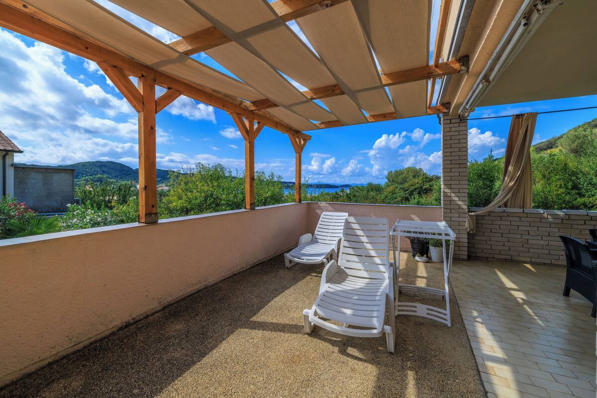 A covered outdoor patio with lounge chairs and a table, overlooking a scenic landscape.