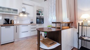 Une cuisine moderne avec des meubles blancs, un four encastré et un îlot central en bois sur lequel se trouve un panier de fruits.