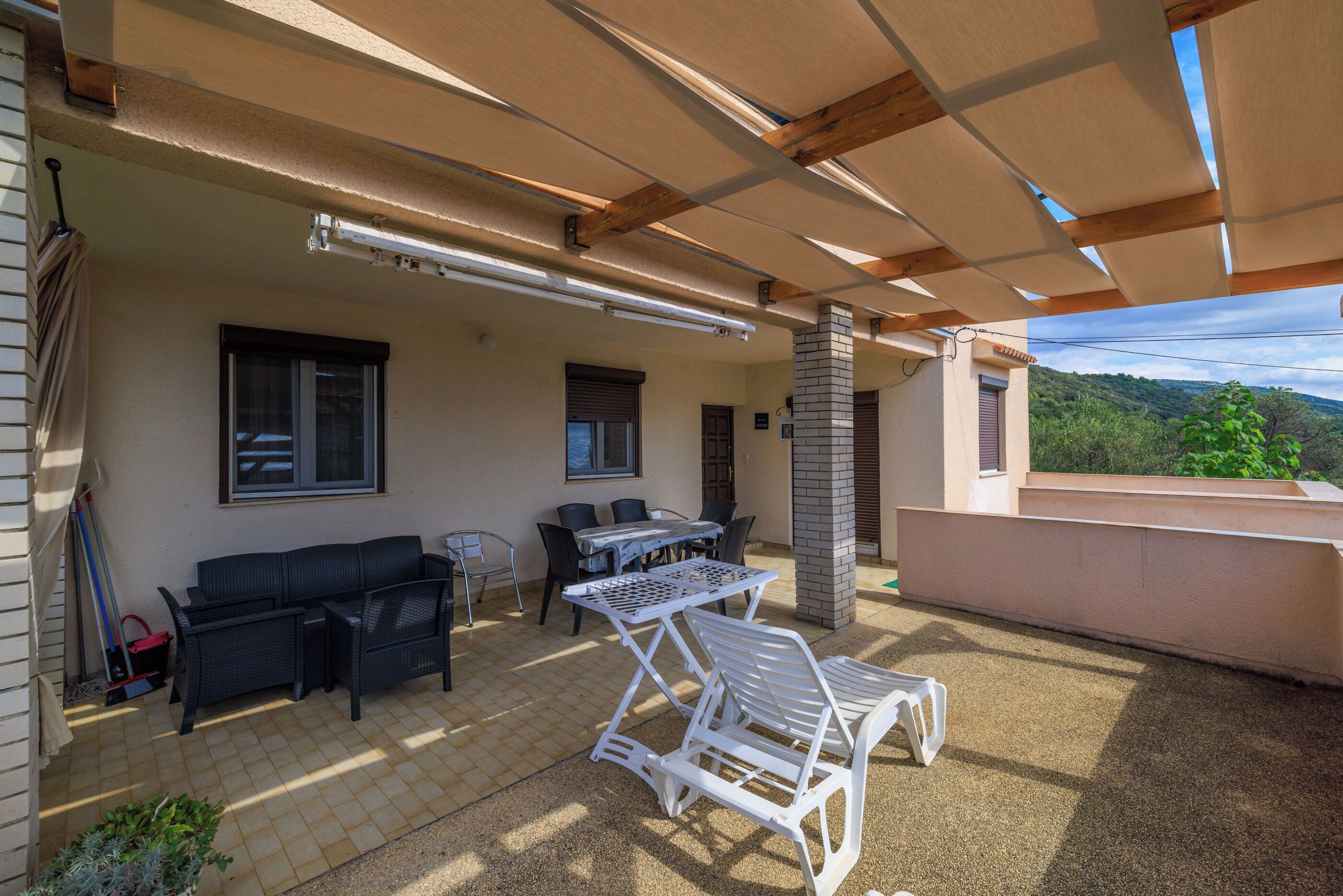 Une terrasse extérieure dotée d’un espace salon couvert, d’une table et d’un fauteuil de relaxation blanc.