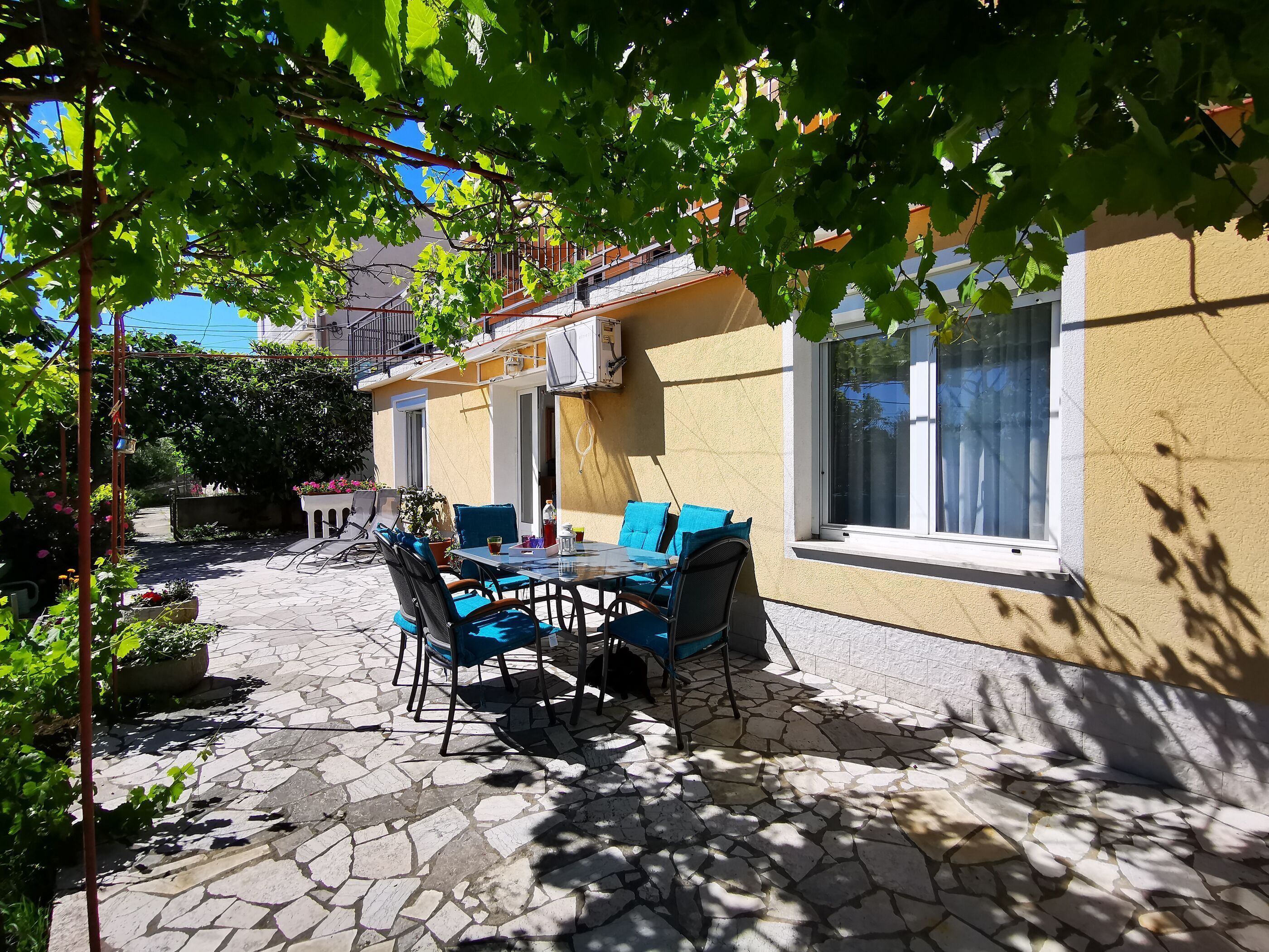 Un patio esterno con un tavolo e sedie, una pianta in vaso e un edificio con una finestra.