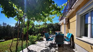 Eine Terrasse mit Steinbelag, Gartenmöbeln und Blick auf Garten und Gebäude.