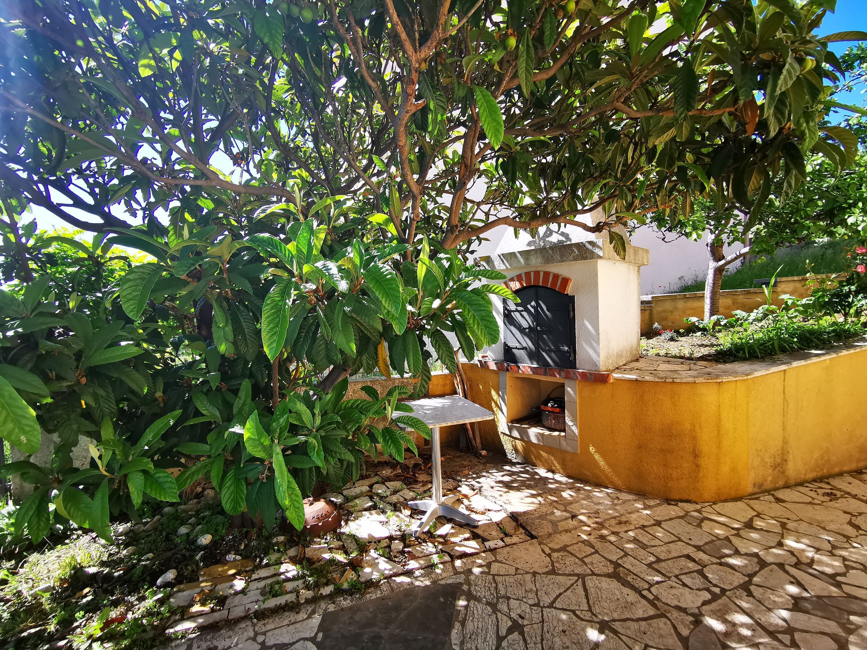 A patio area with a stone-tiled floor, a small table, and a brick oven.