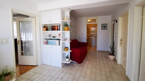 Ein Wohnzimmer mit weißem Bücherregal, einem roten Sofa und einem Fliesenboden.