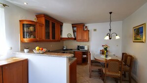 Eine Küche mit Holzausstattung, einem Essbereich mit Tisch und Stühlen sowie einer kleinen Kochinsel mit Obstschale.