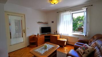 Una sala de estar con televisor, muebles de madera, una ventana con cortinas e iluminación en el techo.