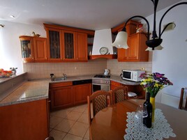 A kitchen with wooden cabinets, a sink, a stove, a microwave, and a dining table with chairs.
