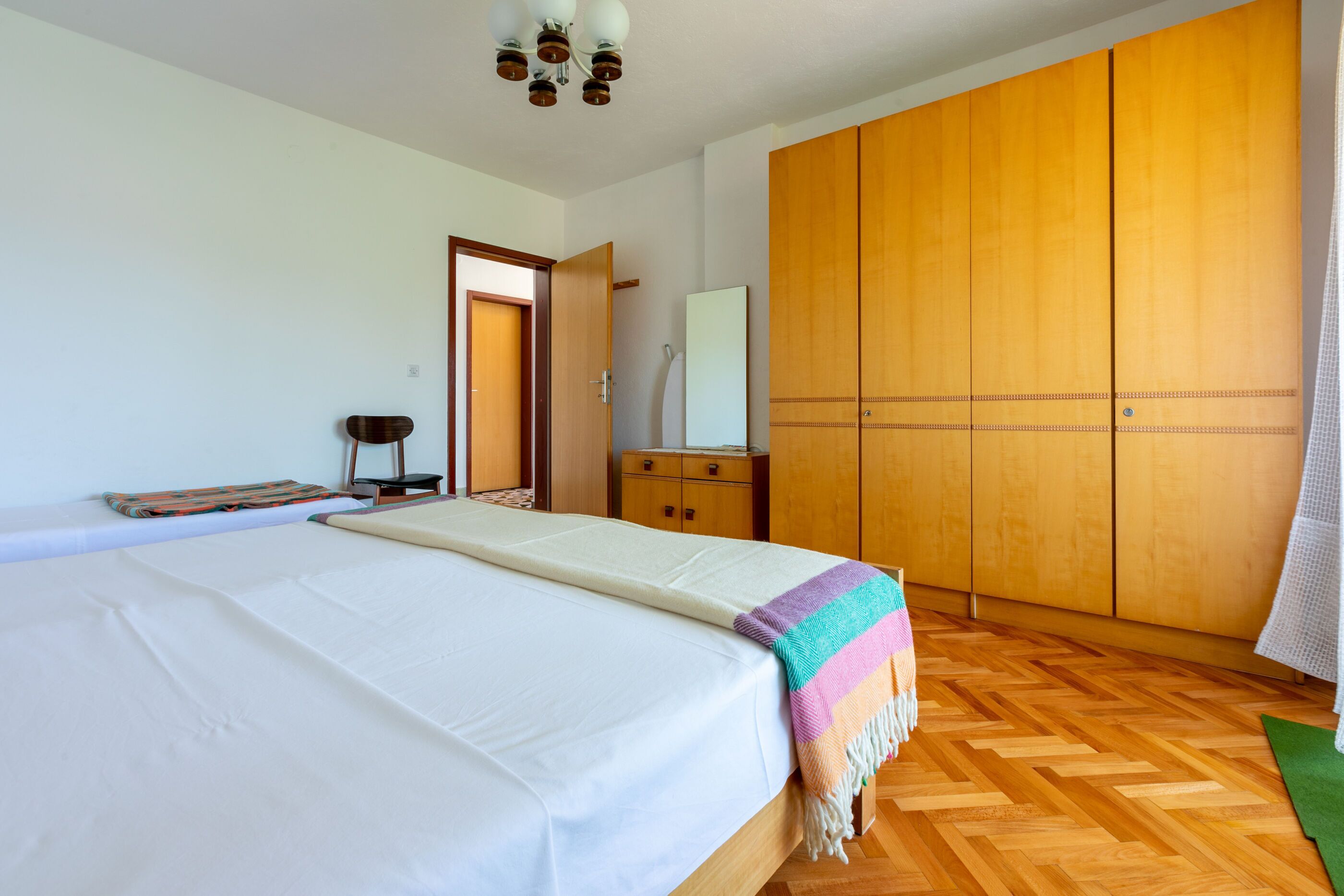 A bedroom with a large bed, wooden wardrobe, and a small bedside table.