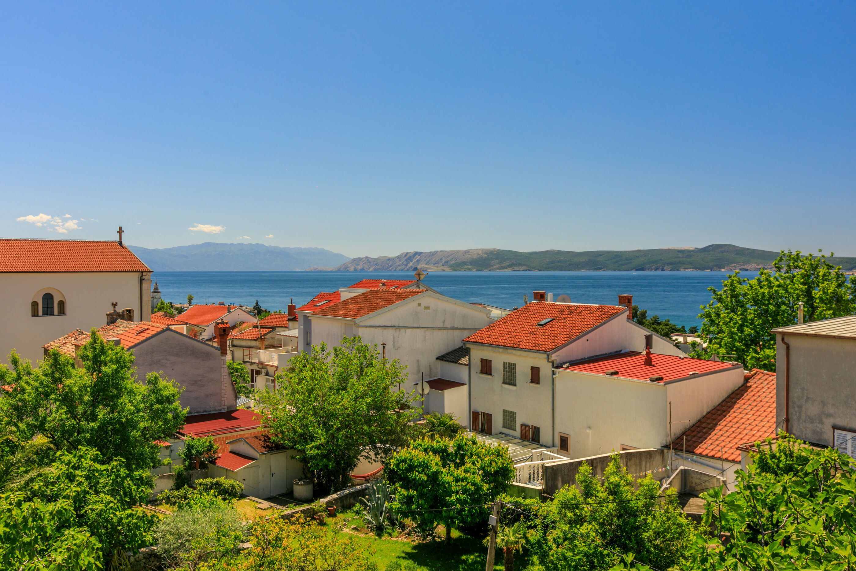 A coastal village with traditional architecture, including buildings with red-tiled roofs and a church with a bell tower.
