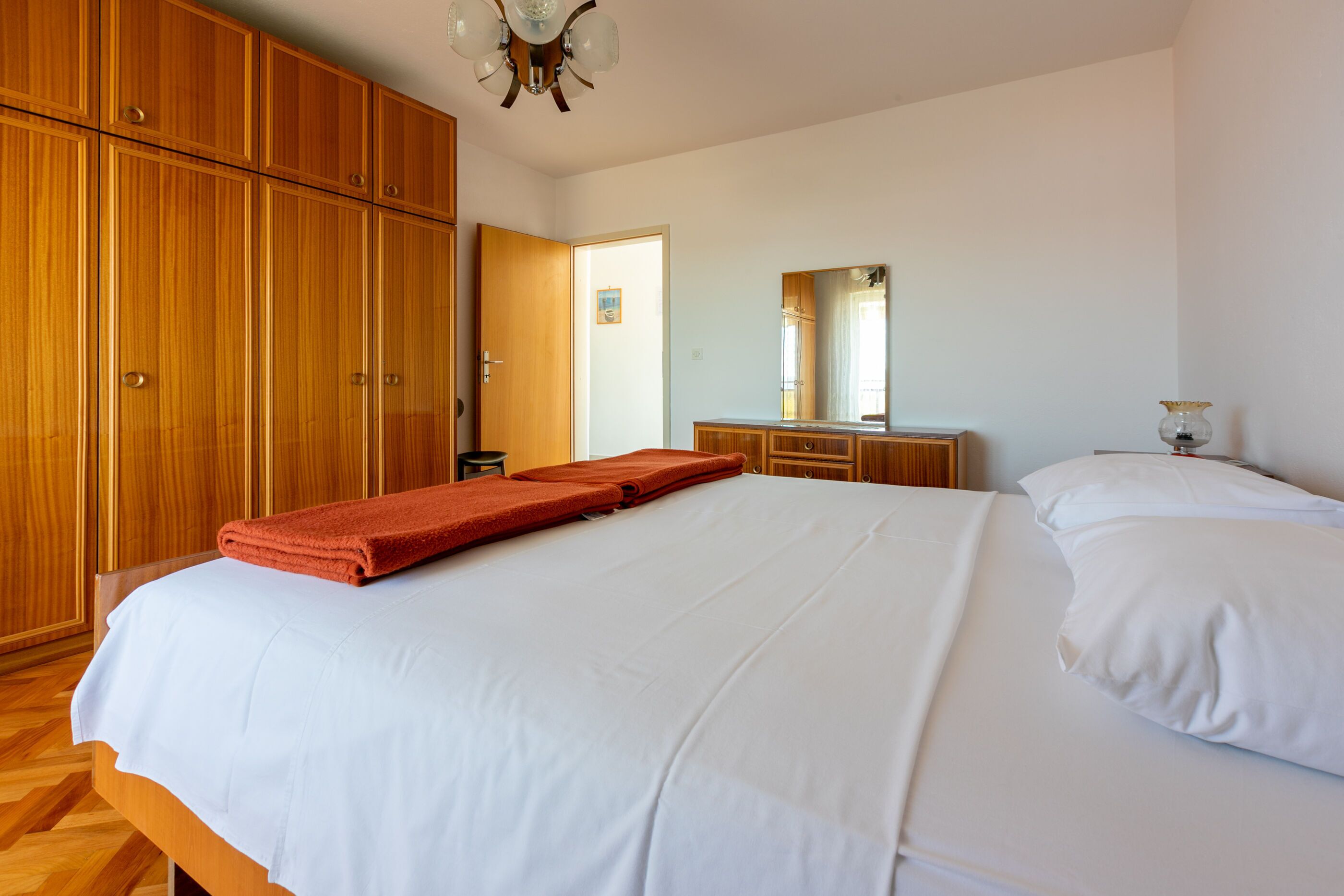 A bedroom with a large bed, wooden wardrobe, and a mirror.
