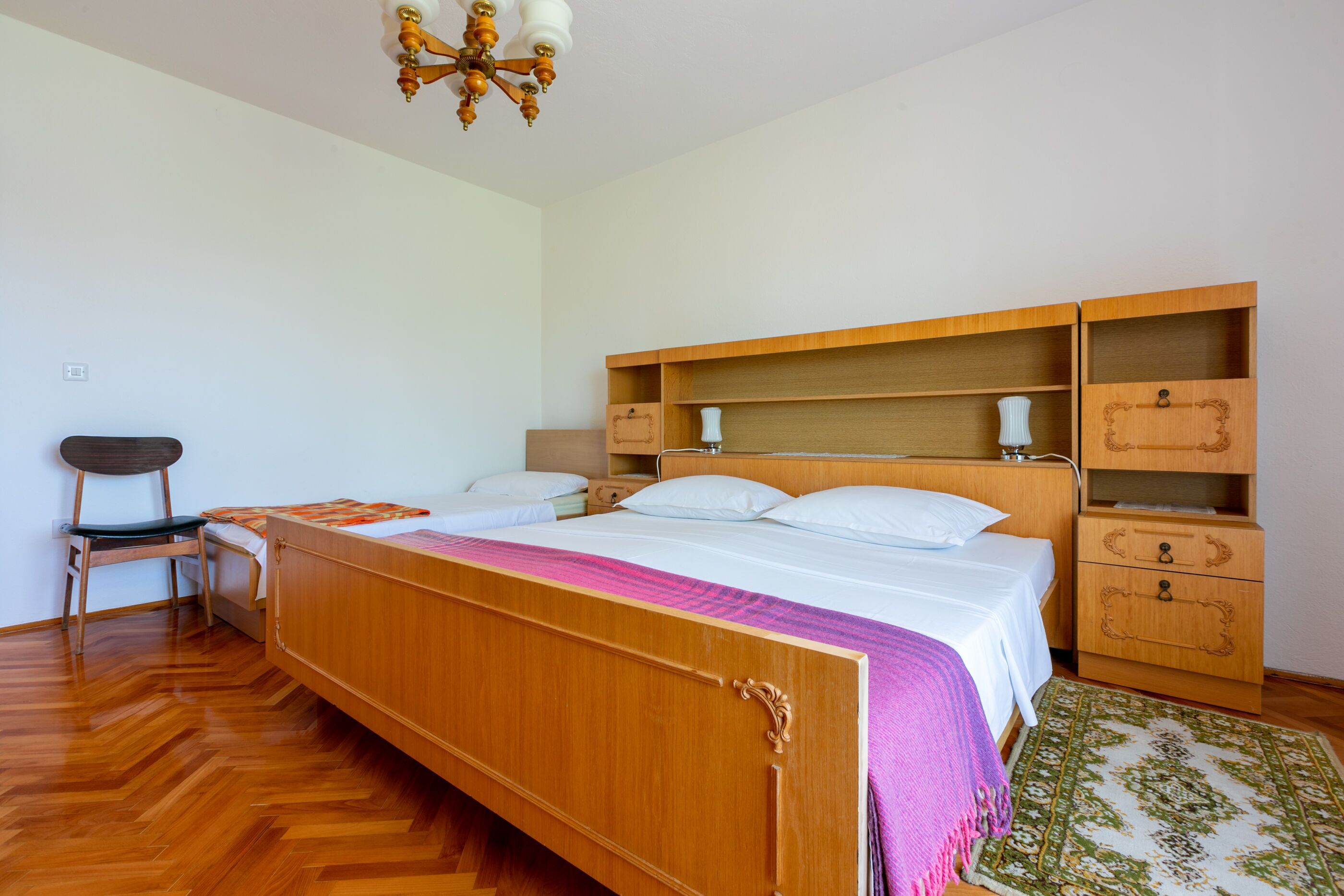 Un dormitorio con cama de madera, una silla, una mesita de noche y un ventilador de techo.