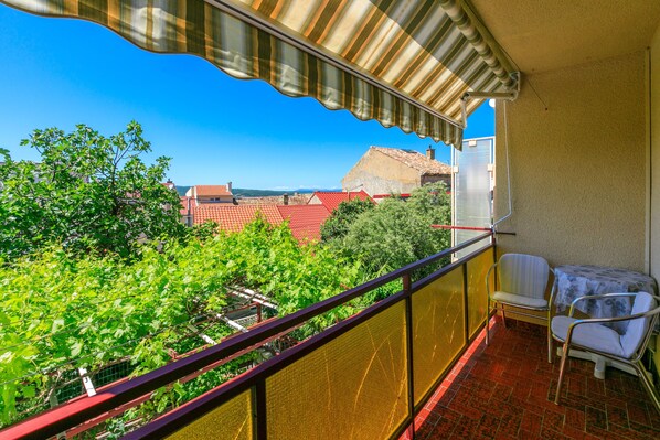A balcony with a view of a red-roofed building, a table with two chairs, and a striped awning. - Apartments Mirena (Crikvenica)