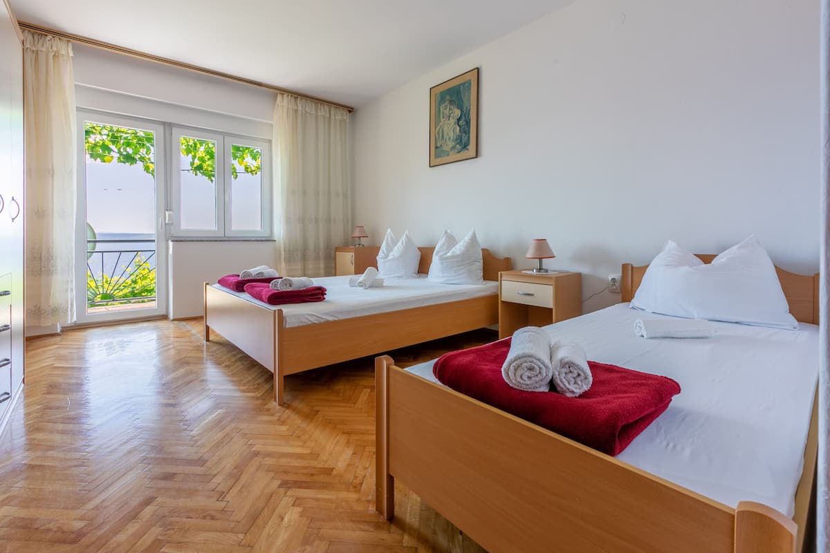 A hotel room with two beds, a balcony with a view, and a painting on the wall.