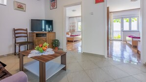 A living room with a wooden table, a TV on a stand, a chair, and a potted plant.