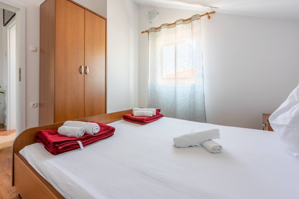 A hotel room with a wooden wardrobe, a bed with white and red towels, and a window with a curtain.