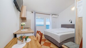 A bedroom with a bed, a wooden table with a vase of flowers, a chair, and a view of the sea through a window.