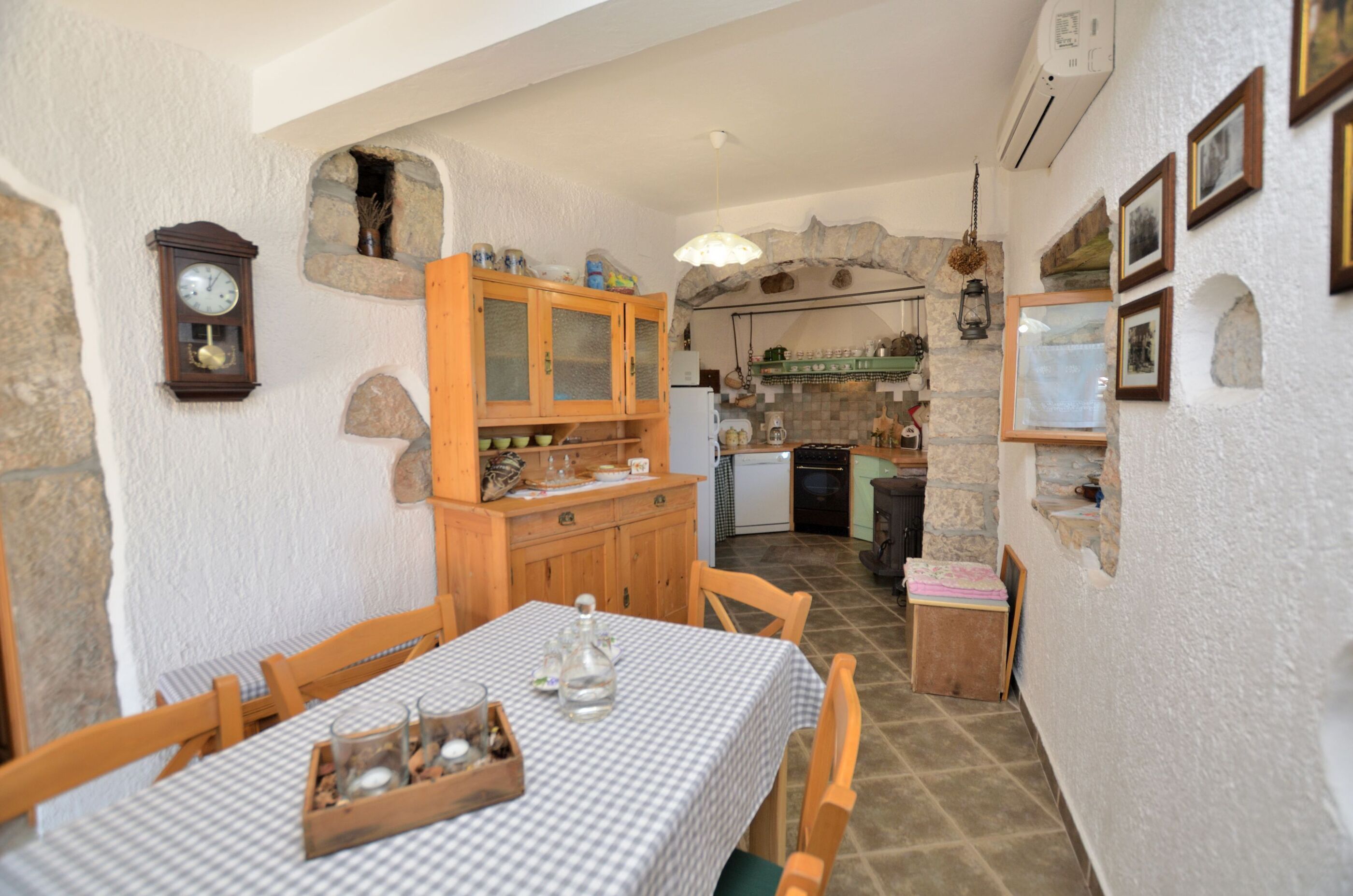 Un coin repas avec une nappe à carreaux, des chaises en bois, un buffet aux portes vitrées et un mur en pierre.