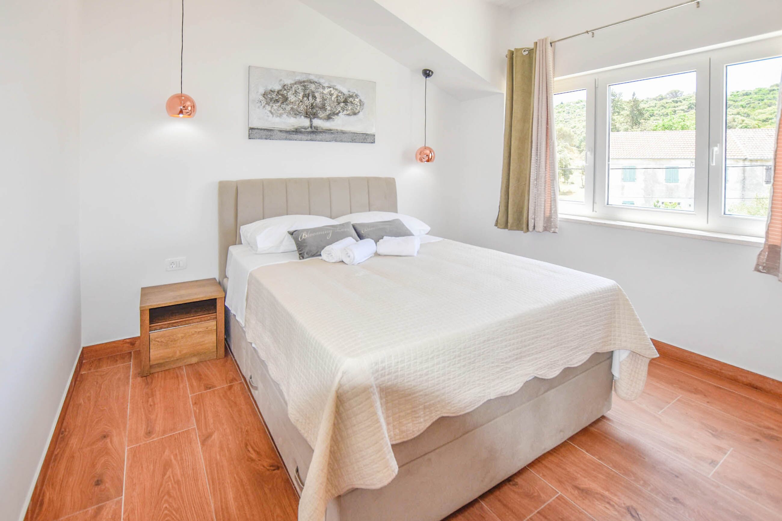 Ein Schlafzimmer mit einem Bett, einem Nachttisch, einem Gemälde und einem Fenster mit Vorhängen.