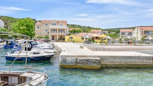 Ein Yachthafen mit vertäuten Booten, einer Betonpier und Gebäuden im Hintergrund mit roten Ziegeldächern.