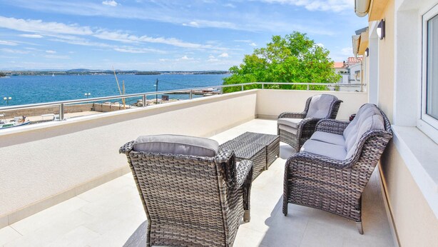 Ein Balkon mit Korbmöbeln, einem Geländer und Blick aufs Meer.