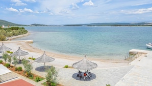 Blick auf einen Strand mit Sonnenschirmen, Fahrrädern und einer Bootsanlegestelle.