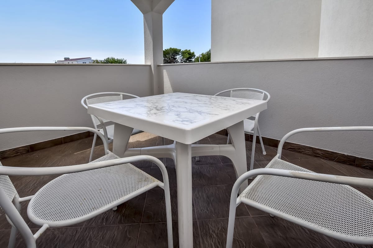Une terrasse avec une table et des chaises blanches, un sol carrelé et une vue sur un bâtiment en arrière-plan.