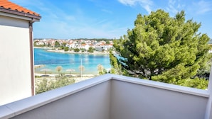 A balcony with a view of a coastal town, clear blue sea, and a pine tree. - Apartments Juro (Rogoznica)