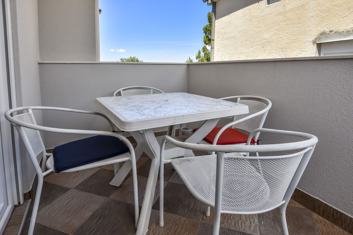 Un balcon avec une table et des chaises blanches, une vue sur le ciel et un bâtiment en arrière-plan.