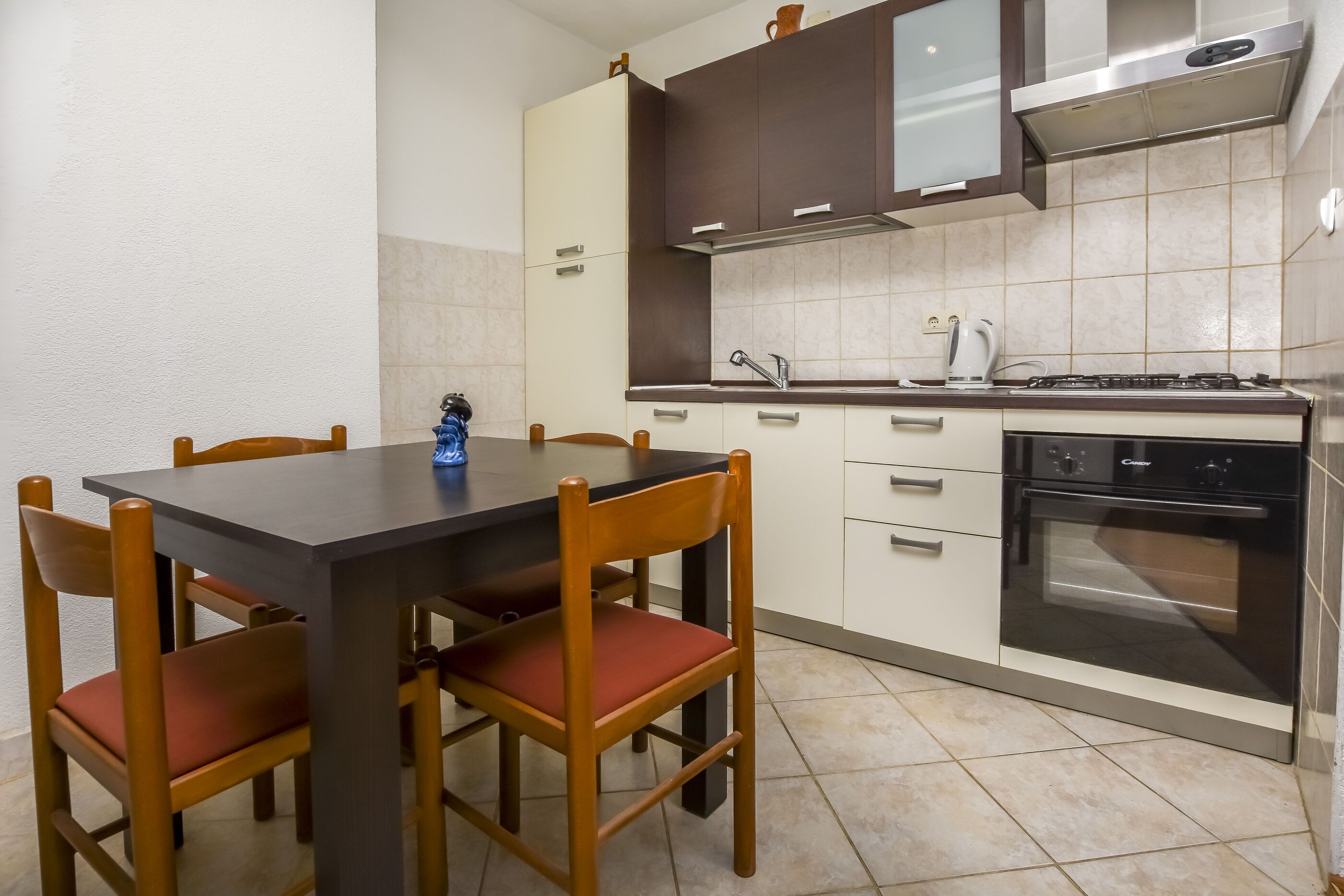 A compact kitchen with a dark countertop, wooden chairs, and a built-in oven.